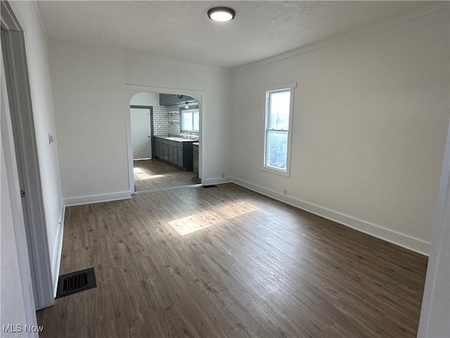 unfurnished living room featuring baseboards, visible vents, arched walkways, and dark wood-style flooring