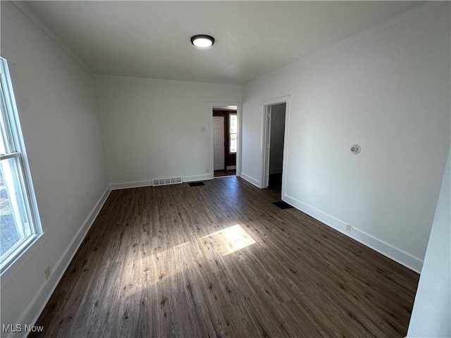 empty room featuring dark wood-style floors, visible vents, and baseboards