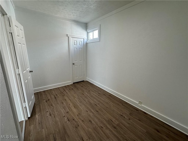 empty room with dark wood finished floors, a textured ceiling, and baseboards