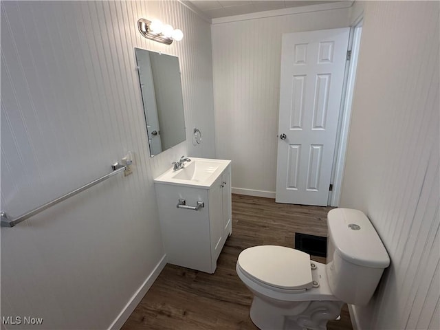 half bath with baseboards, vanity, toilet, and wood finished floors