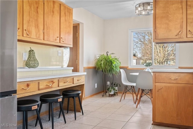 interior space featuring stainless steel refrigerator, tasteful backsplash, light countertops, light tile patterned floors, and baseboards