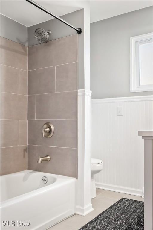 full bath with tile patterned flooring, a wainscoted wall, toilet, and washtub / shower combination