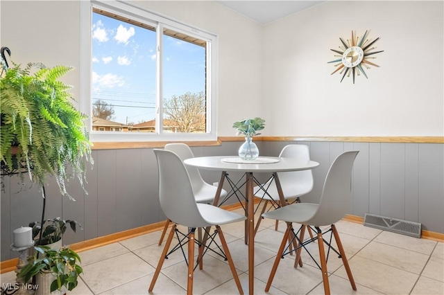 dining area with light tile patterned floors, visible vents, and wainscoting