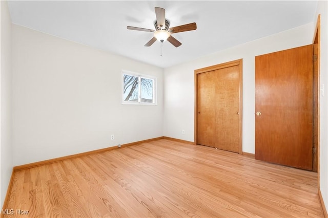 unfurnished bedroom featuring ceiling fan, baseboards, light wood-type flooring, and multiple closets