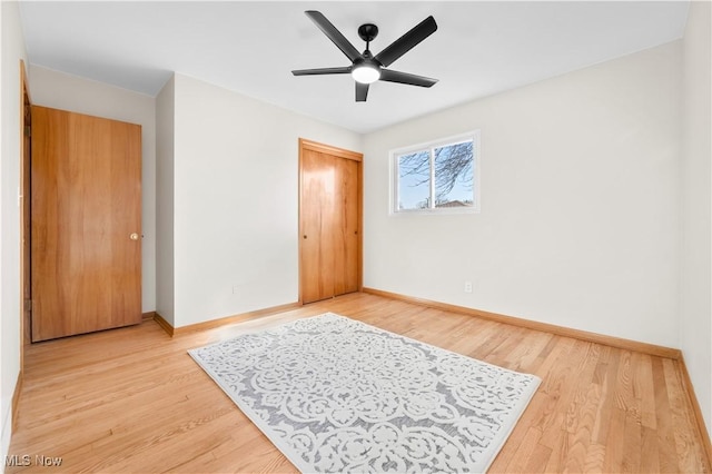 bedroom with a closet, baseboards, light wood-style floors, and ceiling fan