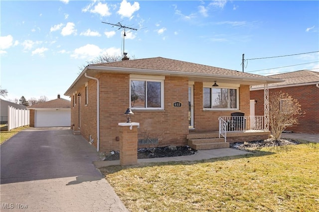 bungalow featuring a detached garage, a porch, an outdoor structure, a front yard, and brick siding