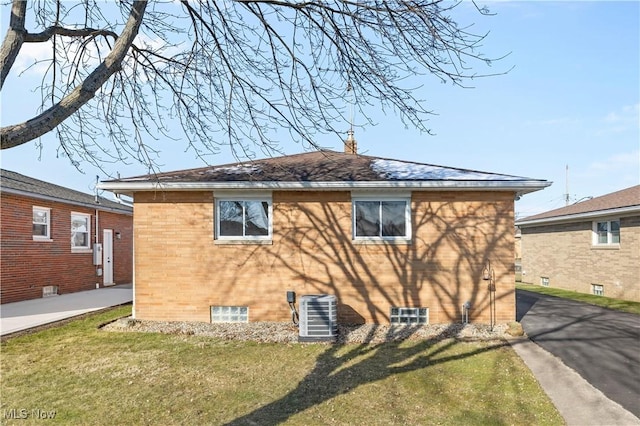 view of side of property with a yard, brick siding, and central AC