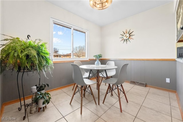 dining space with light tile patterned floors, visible vents, and a wainscoted wall