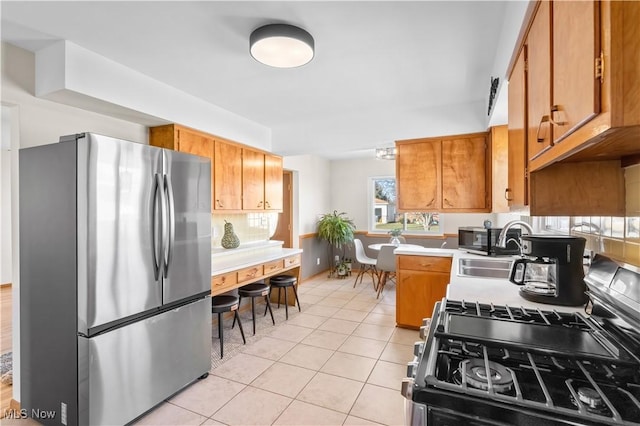 kitchen with light countertops, brown cabinets, light tile patterned flooring, stainless steel appliances, and a sink