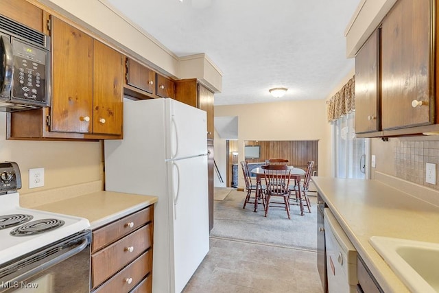 kitchen featuring brown cabinets, tasteful backsplash, light countertops, a sink, and white appliances