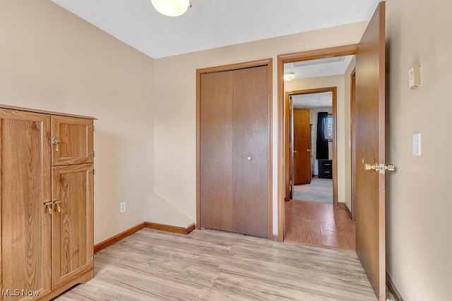 unfurnished bedroom featuring a closet, light wood-type flooring, and baseboards