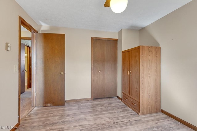 unfurnished bedroom featuring baseboards, a ceiling fan, a textured ceiling, light wood-type flooring, and a closet