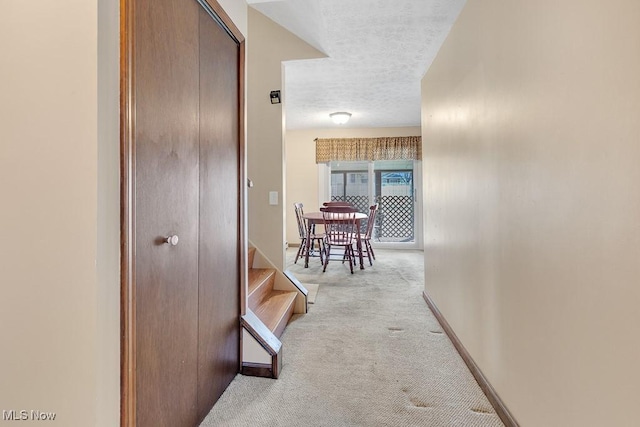 hall featuring carpet floors, a textured ceiling, baseboards, and stairs