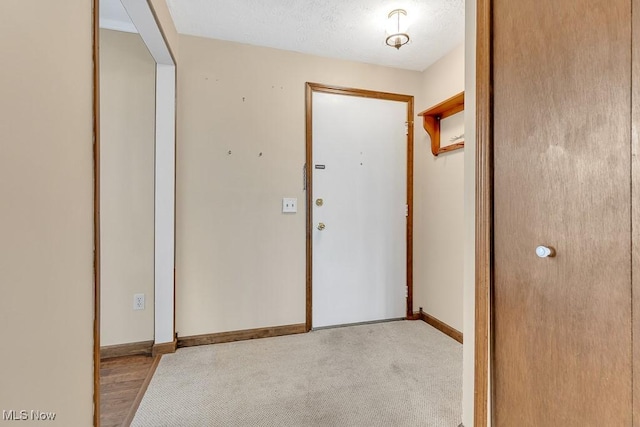 carpeted foyer entrance with a textured ceiling and baseboards