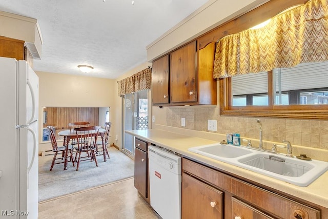 kitchen with white appliances, decorative backsplash, brown cabinets, light countertops, and a sink