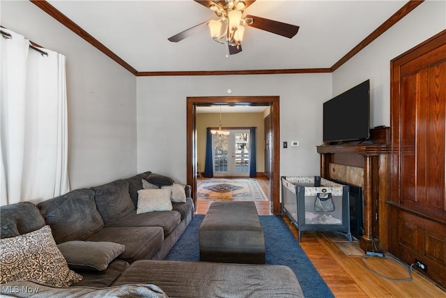 living room featuring ceiling fan, a fireplace with flush hearth, wood finished floors, crown molding, and french doors