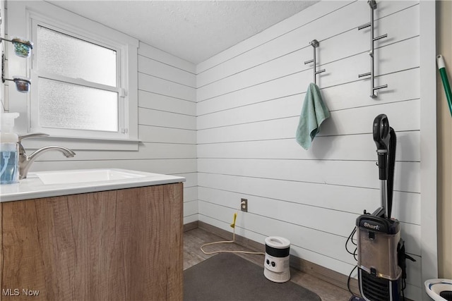 bathroom featuring baseboards, wood walls, a textured ceiling, and vanity