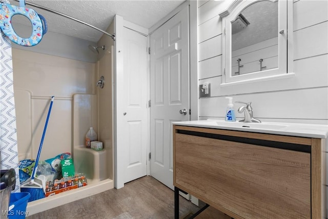 bathroom with a textured ceiling, wood finished floors, walk in shower, and vanity