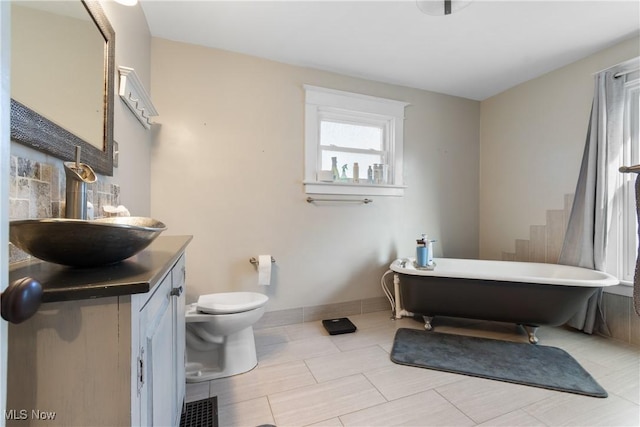 full bath with a freestanding tub, baseboards, vanity, and toilet