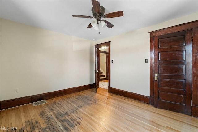 empty room with visible vents, stairway, light wood-style flooring, a ceiling fan, and baseboards