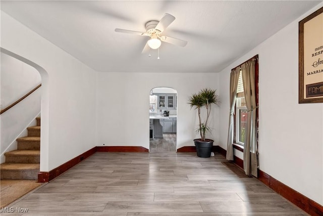 unfurnished room featuring baseboards, light wood-style flooring, arched walkways, and a ceiling fan