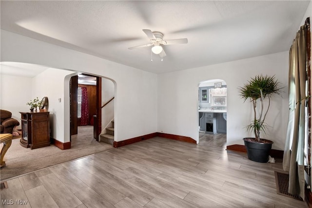 living room featuring visible vents, arched walkways, ceiling fan, stairway, and light wood-type flooring