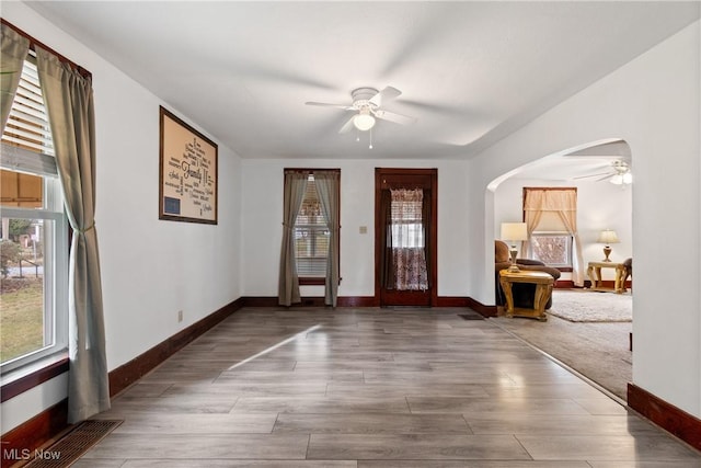 foyer with arched walkways, wood finished floors, a ceiling fan, and baseboards