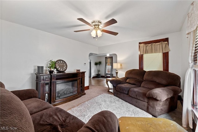 living area featuring arched walkways, carpet, a glass covered fireplace, and a ceiling fan