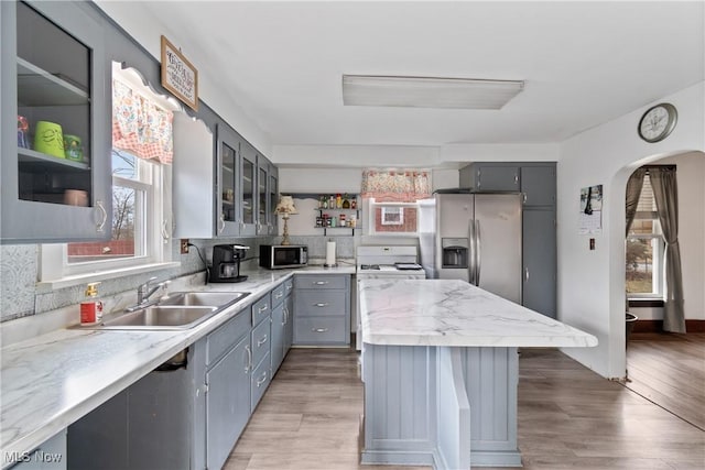 kitchen with arched walkways, gray cabinetry, stainless steel appliances, a sink, and tasteful backsplash