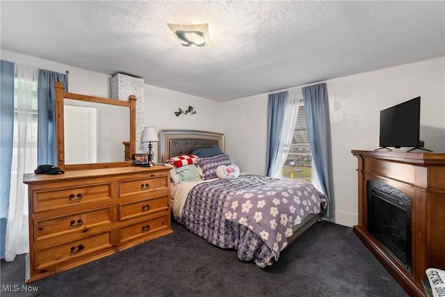 bedroom with dark colored carpet, a fireplace, and a textured ceiling