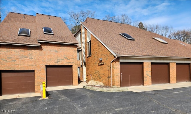 exterior space featuring brick siding, a shingled roof, and community garages