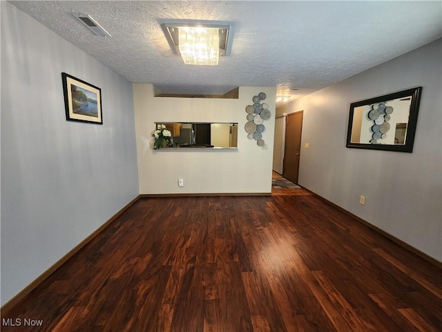 unfurnished room with a textured ceiling, wood finished floors, visible vents, and baseboards