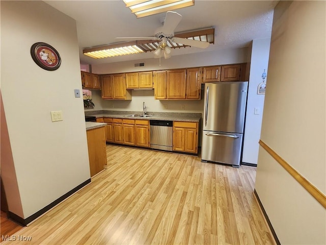 kitchen featuring light wood finished floors, ceiling fan, appliances with stainless steel finishes, brown cabinets, and a sink