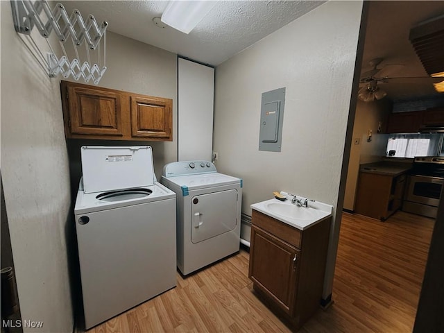 clothes washing area featuring washing machine and clothes dryer, cabinet space, light wood-style flooring, a sink, and electric panel