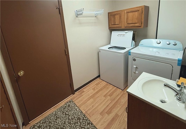 laundry room with light wood-type flooring, independent washer and dryer, a sink, and baseboards