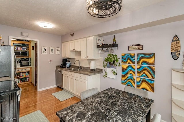 kitchen featuring stainless steel appliances, backsplash, light wood-style flooring, white cabinets, and a sink