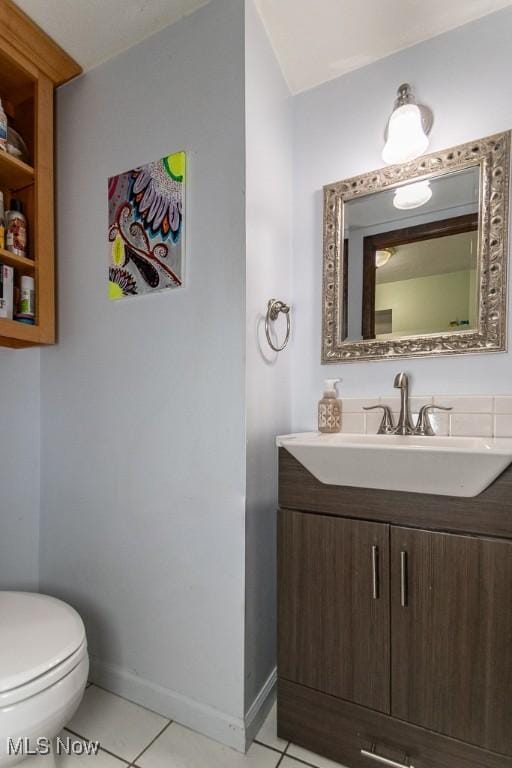 half bathroom with tile patterned flooring, toilet, vanity, and baseboards