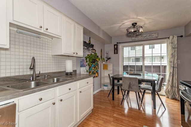 kitchen with a textured ceiling, a sink, white cabinetry, light wood-type flooring, and backsplash