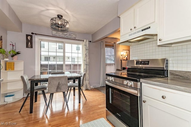 kitchen featuring light wood finished floors, stainless steel electric stove, under cabinet range hood, white cabinetry, and backsplash