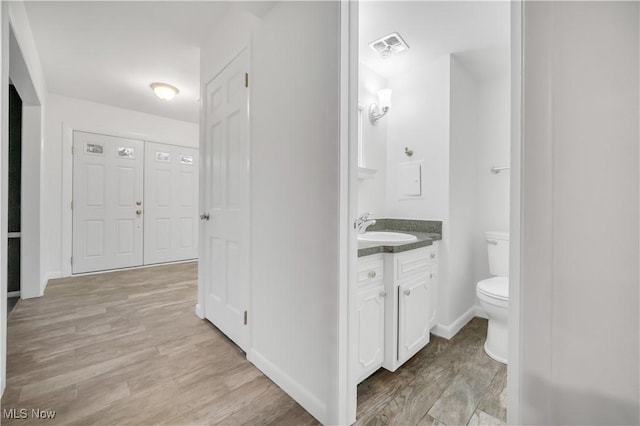 bathroom featuring toilet, wood finished floors, visible vents, vanity, and baseboards