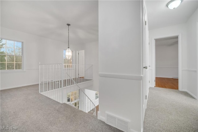 corridor with carpet floors, baseboards, visible vents, and an upstairs landing