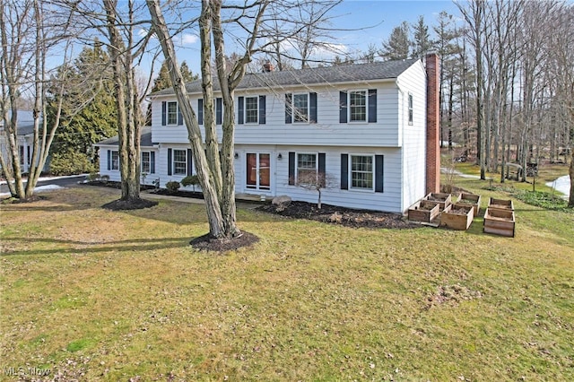 colonial-style house featuring a front lawn, a chimney, and a vegetable garden