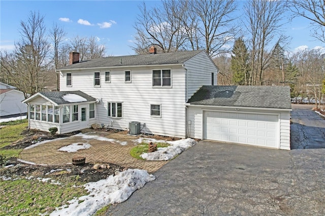 rear view of property featuring central AC unit, a garage, a sunroom, driveway, and a chimney