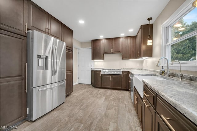 kitchen featuring dark brown cabinetry, stainless steel appliances, a sink, light wood-style floors, and light countertops