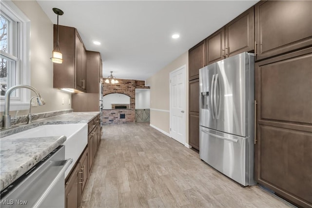 kitchen featuring decorative light fixtures, appliances with stainless steel finishes, light wood-style floors, a sink, and brick wall