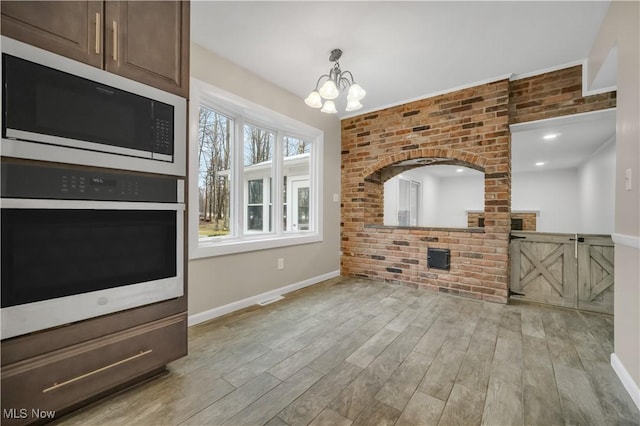 living room with a chandelier, light wood-type flooring, baseboards, and brick wall