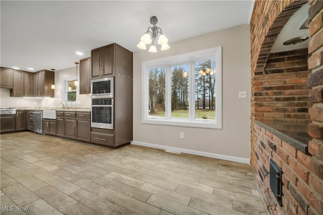 kitchen featuring decorative light fixtures, light countertops, appliances with stainless steel finishes, a sink, and baseboards