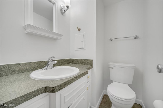 half bathroom featuring toilet, baseboards, and vanity