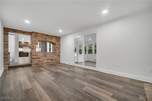 unfurnished living room with brick wall, recessed lighting, wood finished floors, and baseboards