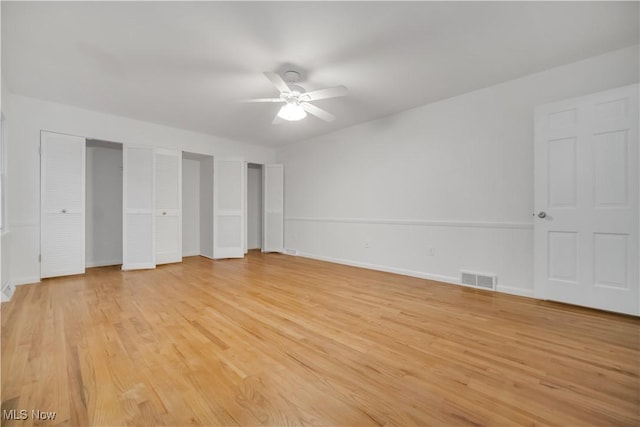 unfurnished bedroom with light wood-style floors, baseboards, visible vents, and two closets